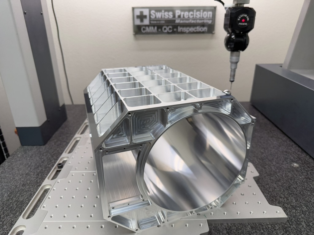 Large machined aluminum housing with a pocketed top and a precision bore, set up on the CMM with the probe head above it.