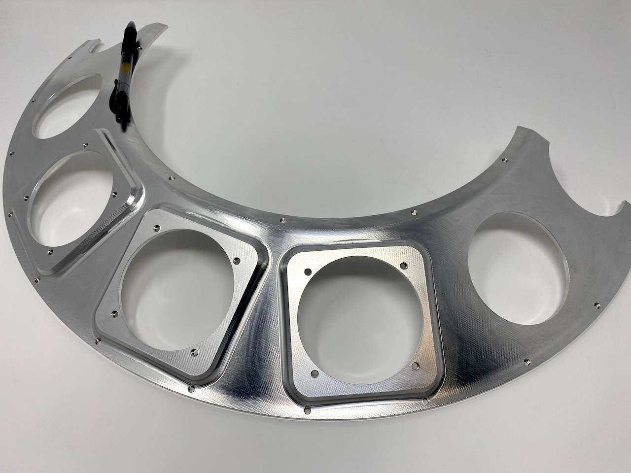 Machined aluminum arc segment with rectangular and round pockets throughout.