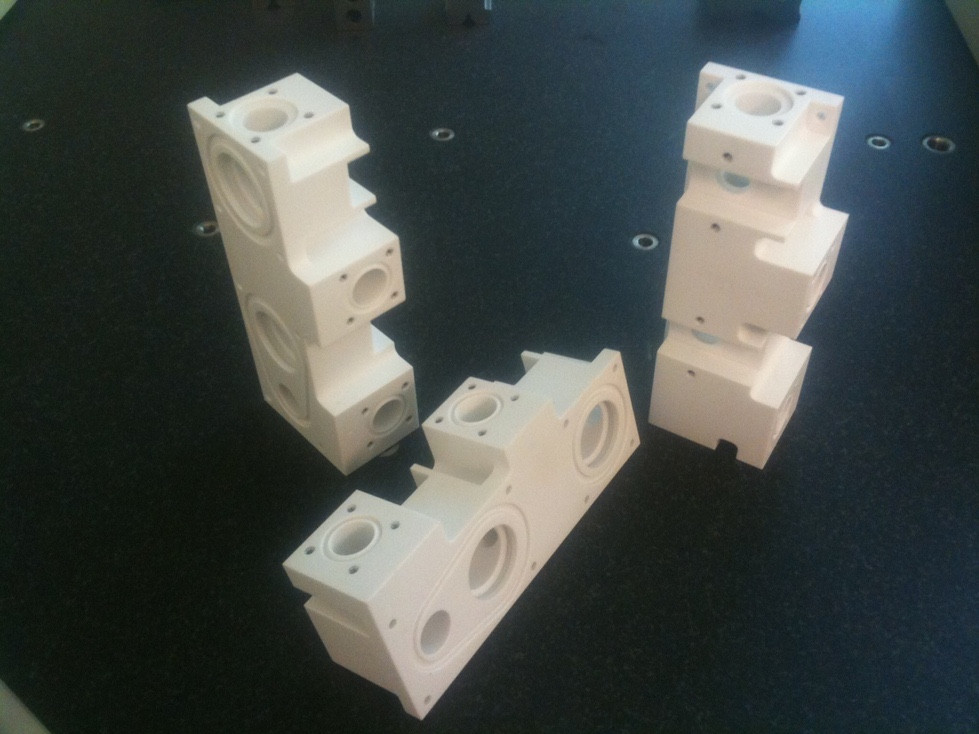 Machined white engineering-plastic blocks with cross-drilled holes and pockets.