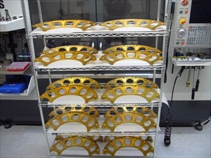 Rack of finished gold-anodized machined frames staged beside the machine.